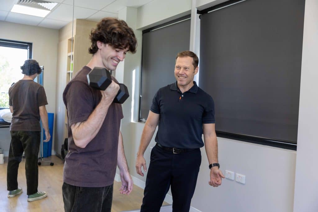 Physiotherapist Dr Duncan Sanders assisting patient with bicep curl dumbbell